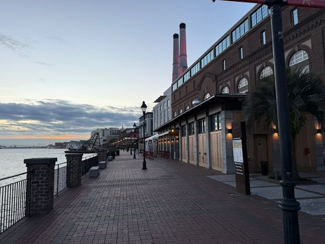 Savannah, Georgia riverfront walkway at dusk featuring brick paths, historic buildings, street lamps, and the river on the left. Home of the 2026 SBS Design Conference.